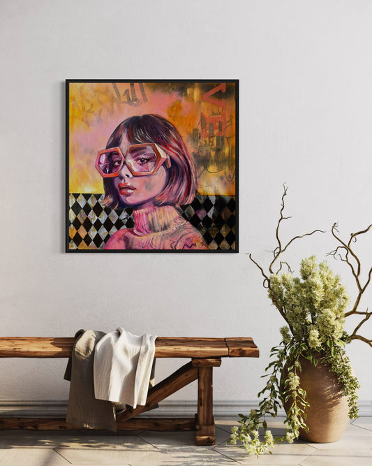 Framed vivid orange and pink portrait artwork of a woman with geometrical shape glasses on a wall above a wooden bench with a blanket.