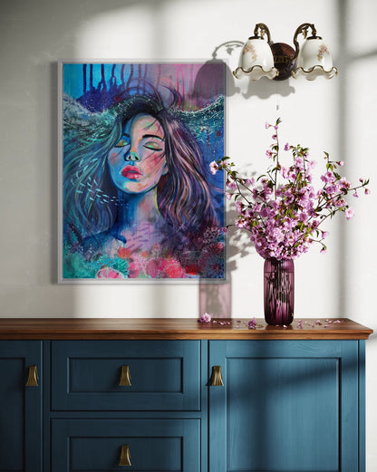 Blue and modern portrait artwork of a woman with long hair in an underwater setting a wall above a blue cabinet with a vase of pink flowers.