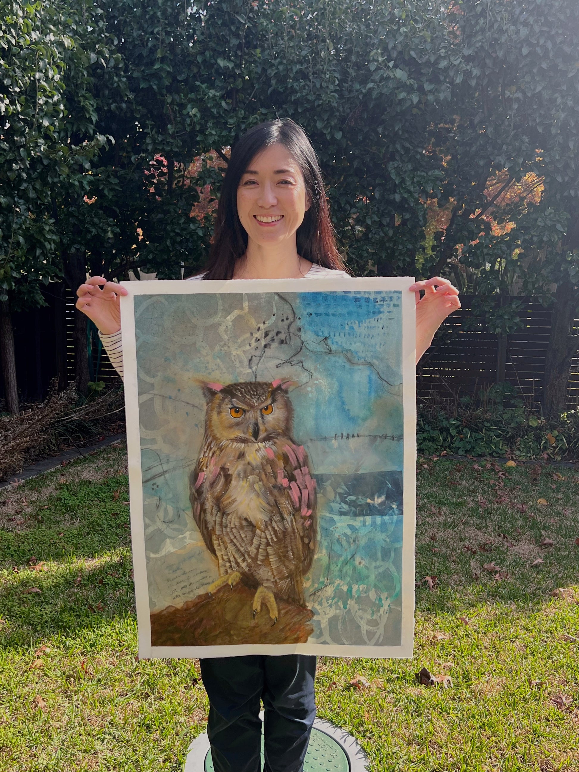 Person holding a contemporary painting of an owl with abstract blue background outdoors