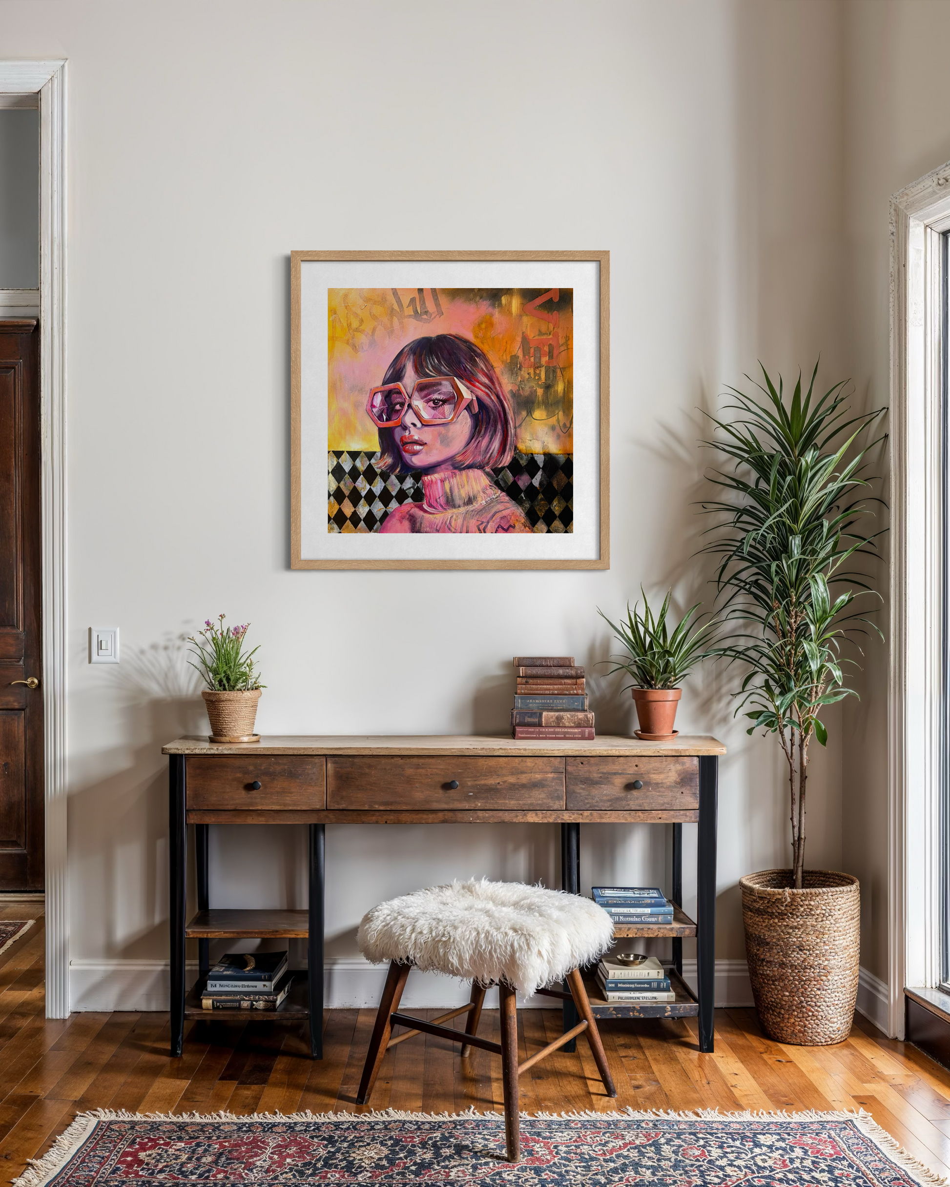 Room interior with a wooden desk, framed artwork of a painting of an  woman with oversized glasses, and decorative plants.