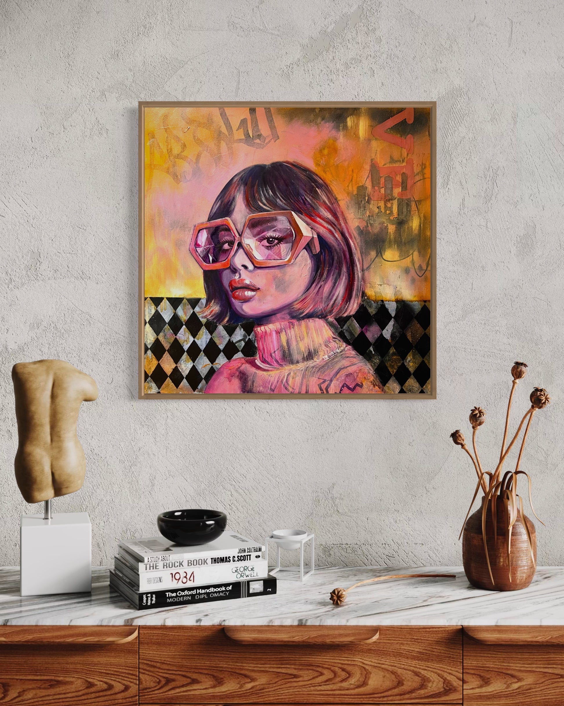 Framed vivid orange and pink portrait artwork of a woman with geometrical shape glasses on a wall above a wooden shelf.