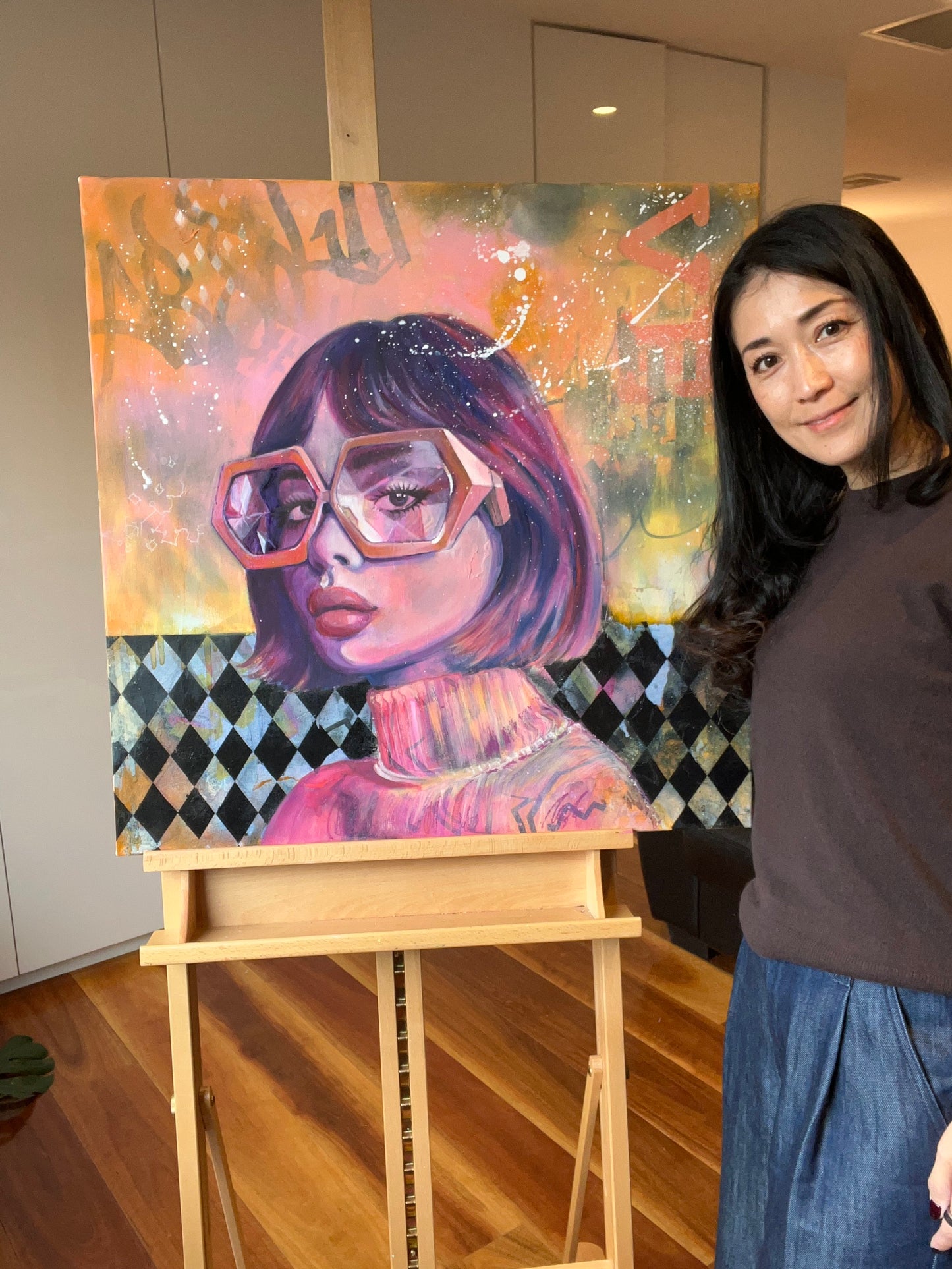 Artist standing next to a colourful painting of a woman with glasses on an easel.