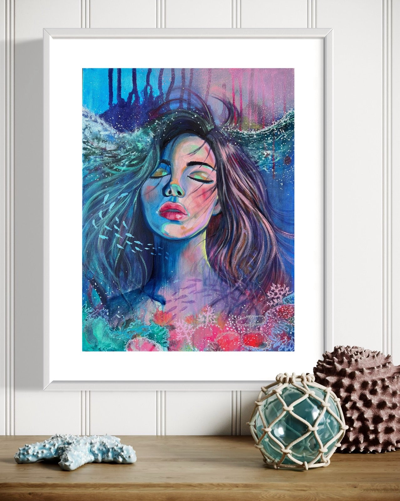Framed blue and modern portrait artwork of a woman with long hair in an underwater setting on a white wall with beach decor